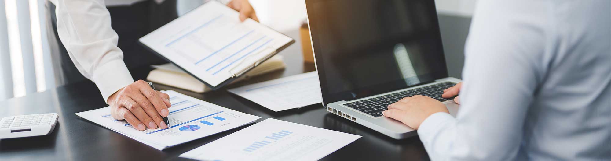 2 people working on desk with laptop and paper reports